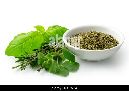 Dried chopped provence herbs in a white ceramic bowl next to fresh bouquet garni isolated on white. Stock Photo