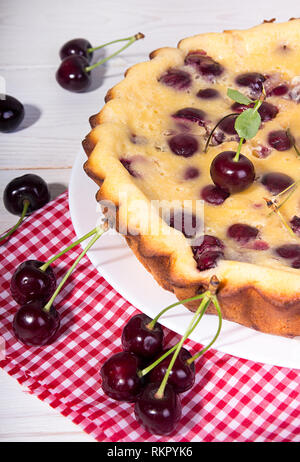 Sweet cherry clafouti on red and white checkered fabric over on white background. Stock Photo