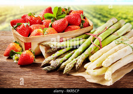 Fresh spring delicacies with white and green asparagus spears and a container of ripe red juicy strawberries outdoors on a farm or garden