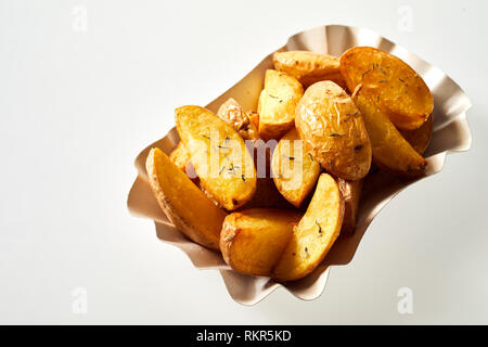 Savory roasted or oven-baked potato wedges seasoned with rosemary and served in a fluted container viewed high angle on white Stock Photo