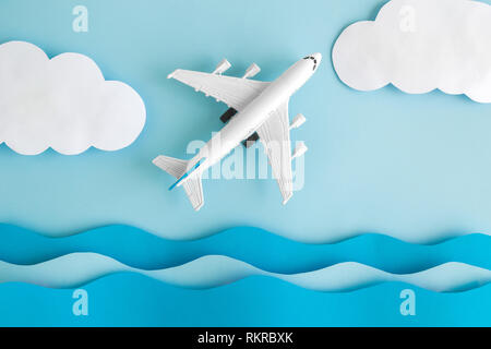 Flat lay of airplane model with sea waves and clouds made of paper against pastel blue background minimal creative travel concept. Stock Photo