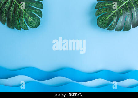 Flat lay of monstera palm leaves and sea waves against pastel blue sky background minimal creative concept. Stock Photo