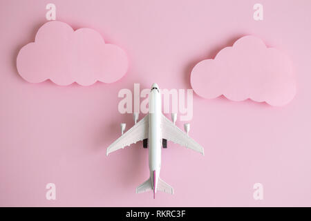 Flat lay of airplane model with pastel pink clouds minimal creative travel concept. Stock Photo