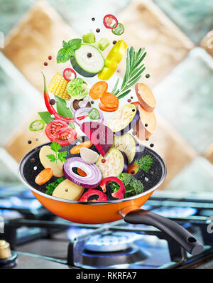 Flying fresh vegetables and spices falling into a pan. Flying motion effect.Gas-stove at the background. Stock Photo