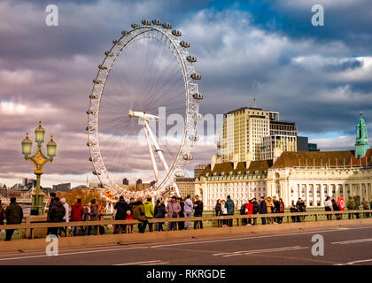 London, UK - January 10, 2019: Tourists visiting London in front of the whell, famous Eye among the Thames river illuminated by sunset light Stock Photo