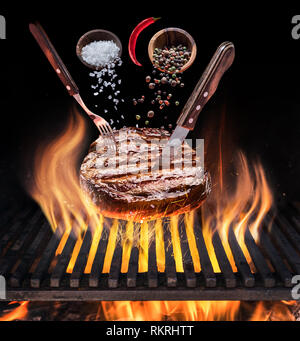 Steak ribeye cooking. Conceptual picture. Steak with spices and cutlery under burning grill grate. Stock Photo