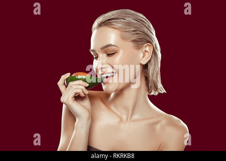 Cheerful blonde-haired model biting avocado while posing with it Stock Photo