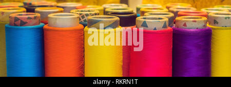 Background with a lot of colorful coils with threads. Bobbins are stacked in three rows, one on the other. The winding is erratic. Multicolored Stock Photo