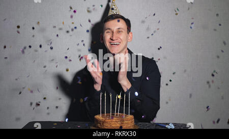 Young man celebrates a holiday, he sits alone at a table with a cake and a candles. Stock Photo