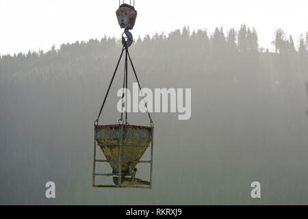 Bucket container with liquid concrete hanging on crane hook on copy space background. Construction machinery equipment. Stock Photo