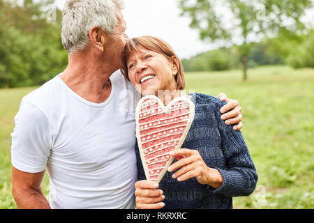 Happy enamored senior couple is standing with a gingerbread heart in the park Stock Photo