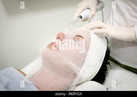 Beautician in white gloves treats  female customer with electric darsonval facial massage, procedure at beauty salon Stock Photo