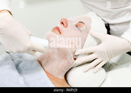 Beautician in white gloves treats  female customer with electric darsonval facial massage, procedure at beauty salon Stock Photo