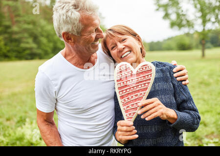 Happy seniors couple with gingerbread heart symbolizing late love Stock Photo