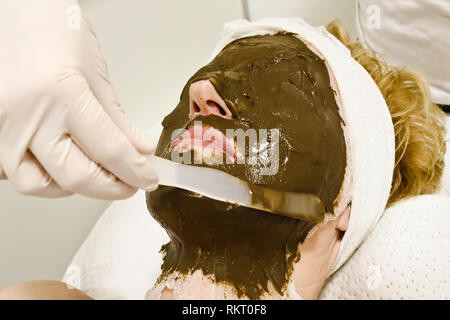 beautician worker applying  cosmetic facial mask of sea algae for anti aging and  hydration of skin  to female client in beauty salon