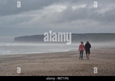 Couple holding hands strolling along the beach on an overcast morning. Hunmanby Gap and North Sea Filey Yorkshire Stock Photo