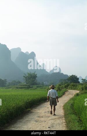 A local man walks along a rural road surrounded by the spectacular scenery of Yangshuo. Speckled with karst mountains and gently flowing rivers, this  Stock Photo