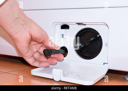 Washing machine filter. Cleaning. Hand takes out a hose. Orange tile Stock Photo