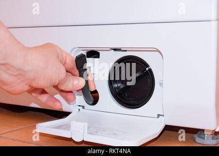Washing machine filter. Cleaning. Hand takes out a hose. Orange tile Stock Photo