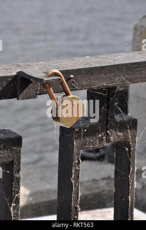 Old rusty padlock hanging on a black bar of an iron parapet covered with cobweb at a river port. Stock Photo