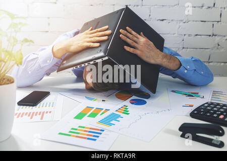 tired overworked office worker sleeping on the desk with laptop over head Stock Photo