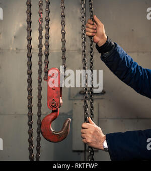 senior man holding metallic chain with red hook in technical room Stock Photo