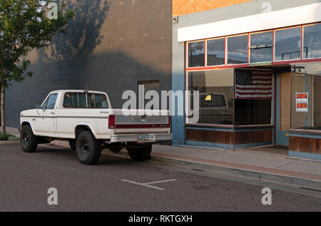 Old Ford pickup truck near closed shop in Winslow, Arizona, United States of America. Store with for sale and for rent sign and American flag on windo Stock Photo
