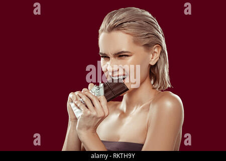 Blonde-haired model with bob cut needing much effort to bite chocolate Stock Photo