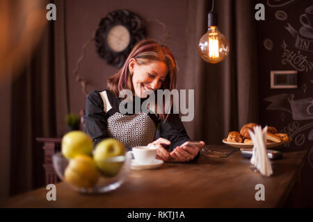 Adult businesswoman laughing while looking at her phone. Recreation in vintage coffee shop Stock Photo
