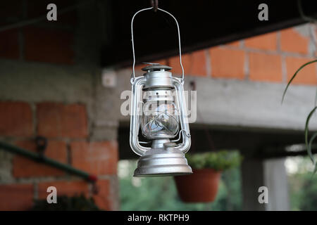 Old rusty oil lamp hanging in a metal hook from a wooden post outdoors Stock Photo