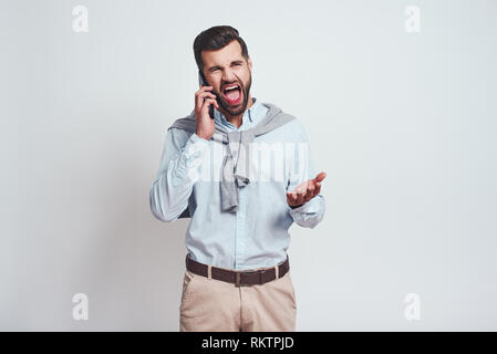 What have you done, oh no. Angry bearded man is screaming while talking with somebody by smartphone. Negative emotions. Grey background. Close up Stock Photo