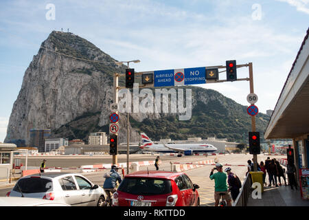 a British Airways Airbus A320 plane takes off on the road while traffic and pedestrians wait, at the famous runway crossing at Gibraltar Airport Stock Photo
