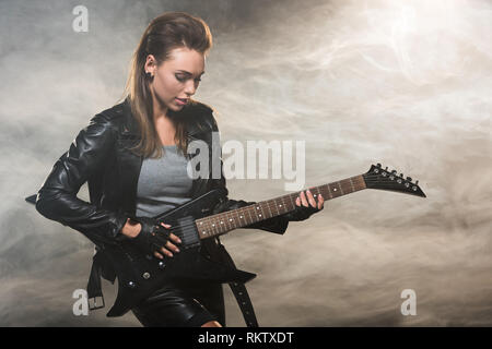 beautiful woman in leather jacket playing electric guitar on smoky background Stock Photo