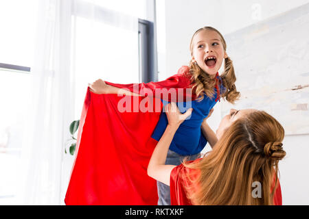 Happy mother and kid in red cloaks playing at home Stock Photo