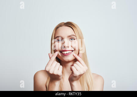 Cute blonde girl is showing  heart sign with her fingers while standing on a grey background. Close-up. Love concept Stock Photo