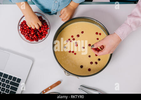 cropped view of mother and child adding cranberries to dough in baking form on white background Stock Photo