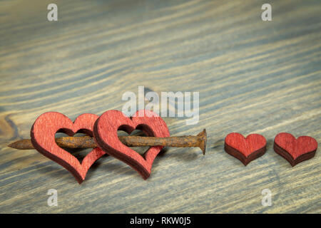 Wooden hearts connected together with small rusted nail. Cut out wooden heart shapes painted red, viewed in close-up on wooden background with copy sp Stock Photo