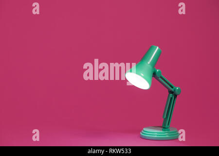 Retro green desk lamp on a bright pink background.  Tuned on and shining on a work surface Stock Photo
