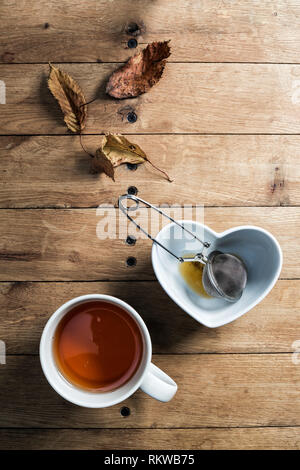 A mug of herbal tea with a steel mesh strainer and autumn leaves table decoration. Stock Photo