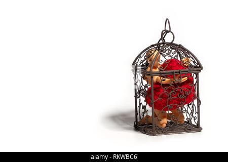 Action figure sitting in cage and holding red heart on white background. Concept of Love and imprisonment Stock Photo