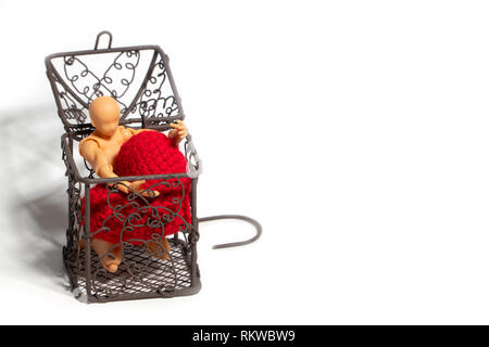 Action figure sitting in cage and holding red heart on white background. Concept of Love and imprisonment Stock Photo