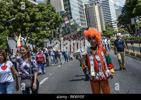 Caracas, Miranda, Venezuela. 12th Feb, 2019. A man wearing a clown costume seen holding a placard during a protest to call for a change in the government.Opponents gather at a protest organised by the PSUV (United Socialist Party of Venezuela) after the call from interim president Juan Guaido, to show their support to him, while asking the army to allow more humanitarian aids into the country. Credit: Roman Camacho/SOPA Images/ZUMA Wire/Alamy Live News Stock Photo