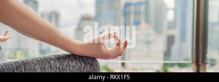 Young woman is practicing yoga in the morning on her balcony with a panoramic view of the city and skyscrapers BANNER long format Stock Photo