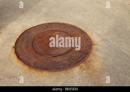 An Isolated rusty man hole cover leading to electrical wiring Stock Photo