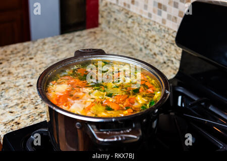 Large big pot of homemade vegetable soup and granite counter top in kitchen in stainless steel container on gas stove cooking and nobody Stock Photo
