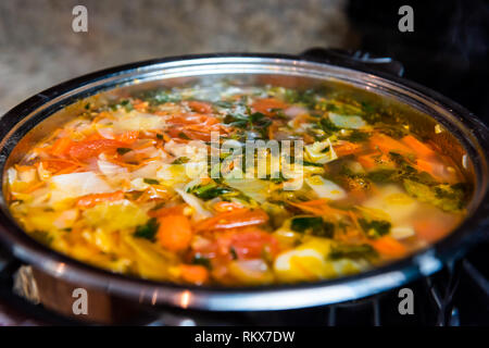 Large big pot of homemade vegetable soup macro closeup in kitchen in stainless steel container on stove cooking and nobody Stock Photo
