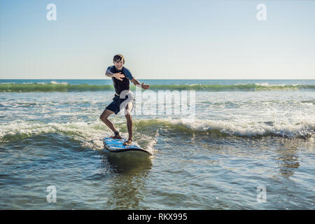 Young man, beginner Surfer learns to surf on a sea foam on the Bali island Stock Photo