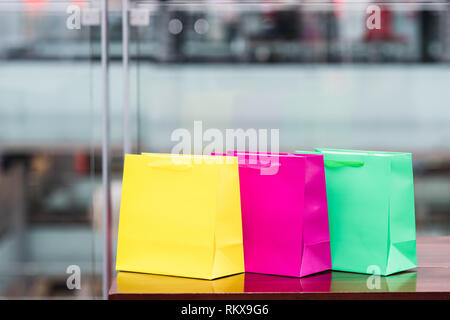 Three colored gift bags in a mall with a defocused background. Stock Photo