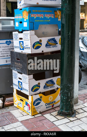 Malaga, Spain - May 19, 2018. empty cardboard boxes bananas and tropical fruits stacked on the street in the city near plastic dumpster Stock Photo