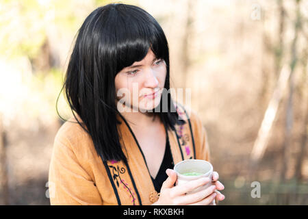 Woman holding matcha green tea cup on outside in backyard garden with young girl black hair and asian clothes looking Stock Photo
